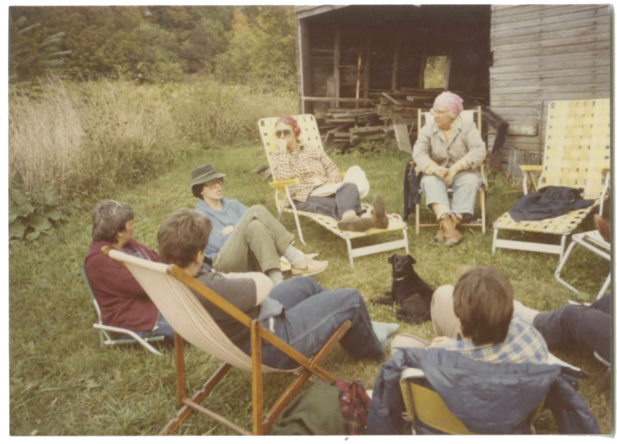 An old photo of seven women sitting in lawn chairs outside in a circle.