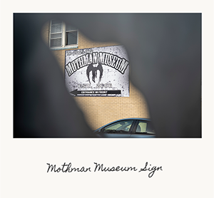 A sign on the wall of a building guiding you to the Mothman Museum